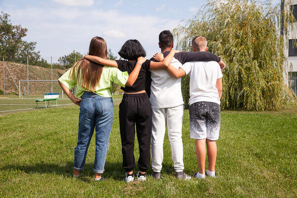 4 Kinder stehen mit dem Rücken zur Kamera und umarmen sich.