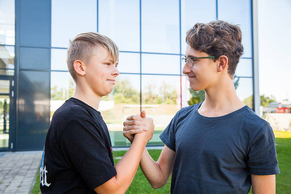 2 Jungs stehen draußen und geben sich einen Handschlag.