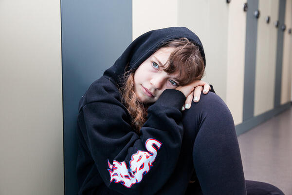Ein trauriges Mädchen sitzt mit einem schwarzen Kapuzenpullover am Gang.