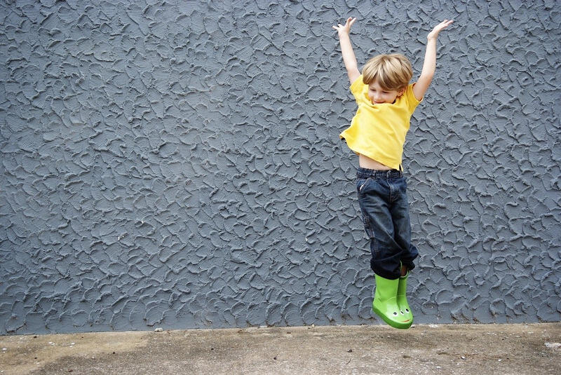 Kleiner Junge mit Gummistiefel hüpft fröhlich.