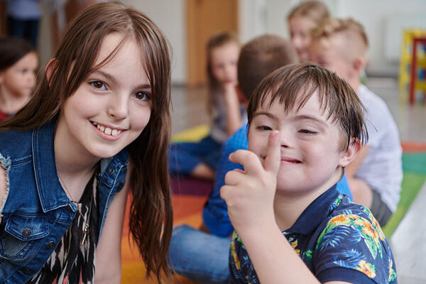 Ein Mädchen und ein Junge mit Down-Syndrom lächeln in die Kamera